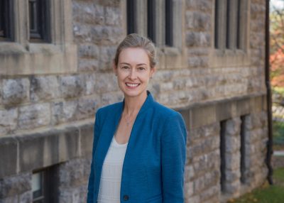portrait of woman in blue blazer outside in front of stone building.