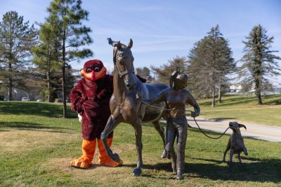 The Virginia Tech Hokie Bird posing in front of the Running Together statue at the Virginia-Maryland College of Veterinary Medicine. 