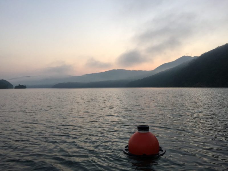 photo of red buoy in a lake at dusk with mountains int he background